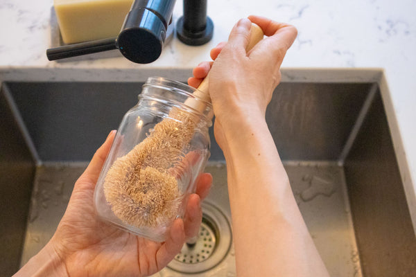 Person using a coconut brush to wash a mason jar