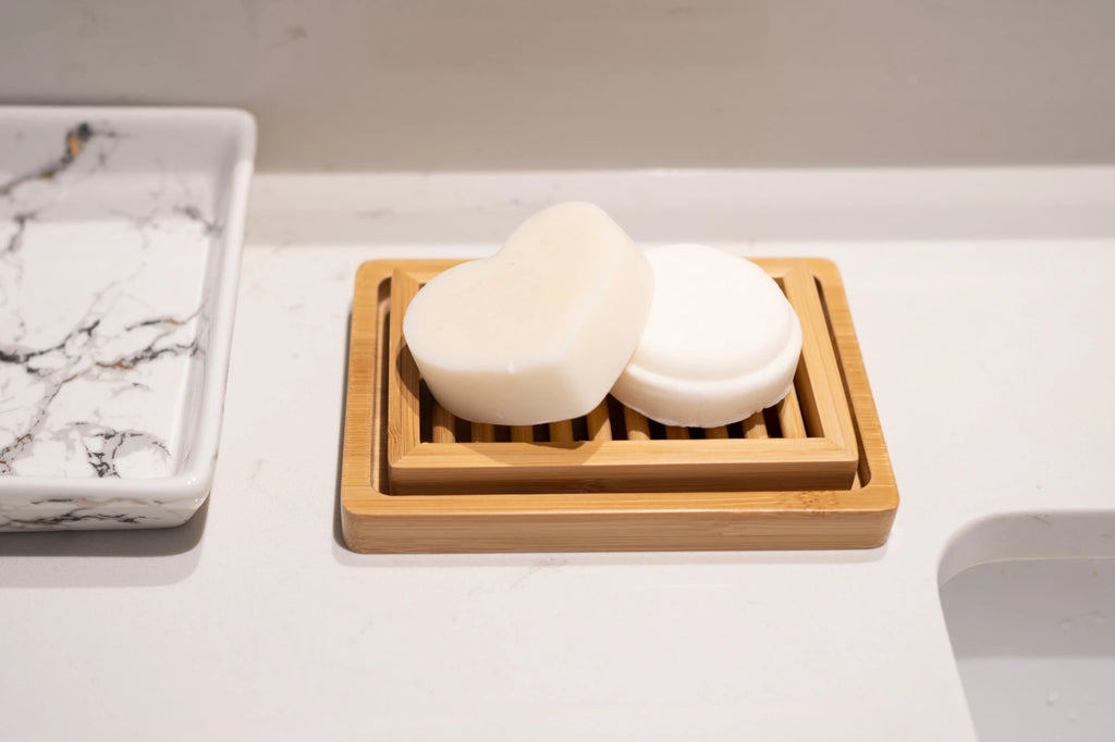 Set of hydrating shampooo and conditioner bars on a bamboo soap dish on a bathroom vanity