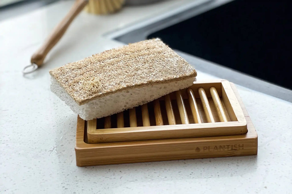 Plant-based sponge on a bamboo soap dish on a white counter next to the kitchen sink