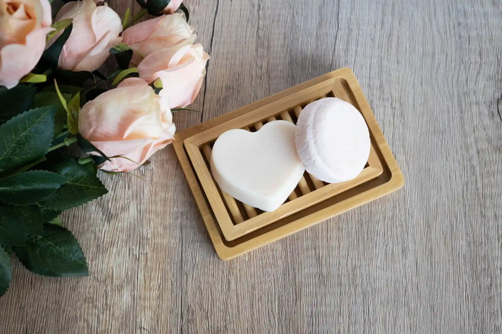 Nourishing shampoo and conditioner bars on a dual-layer bamboo soap dish next to a bouquet of roses