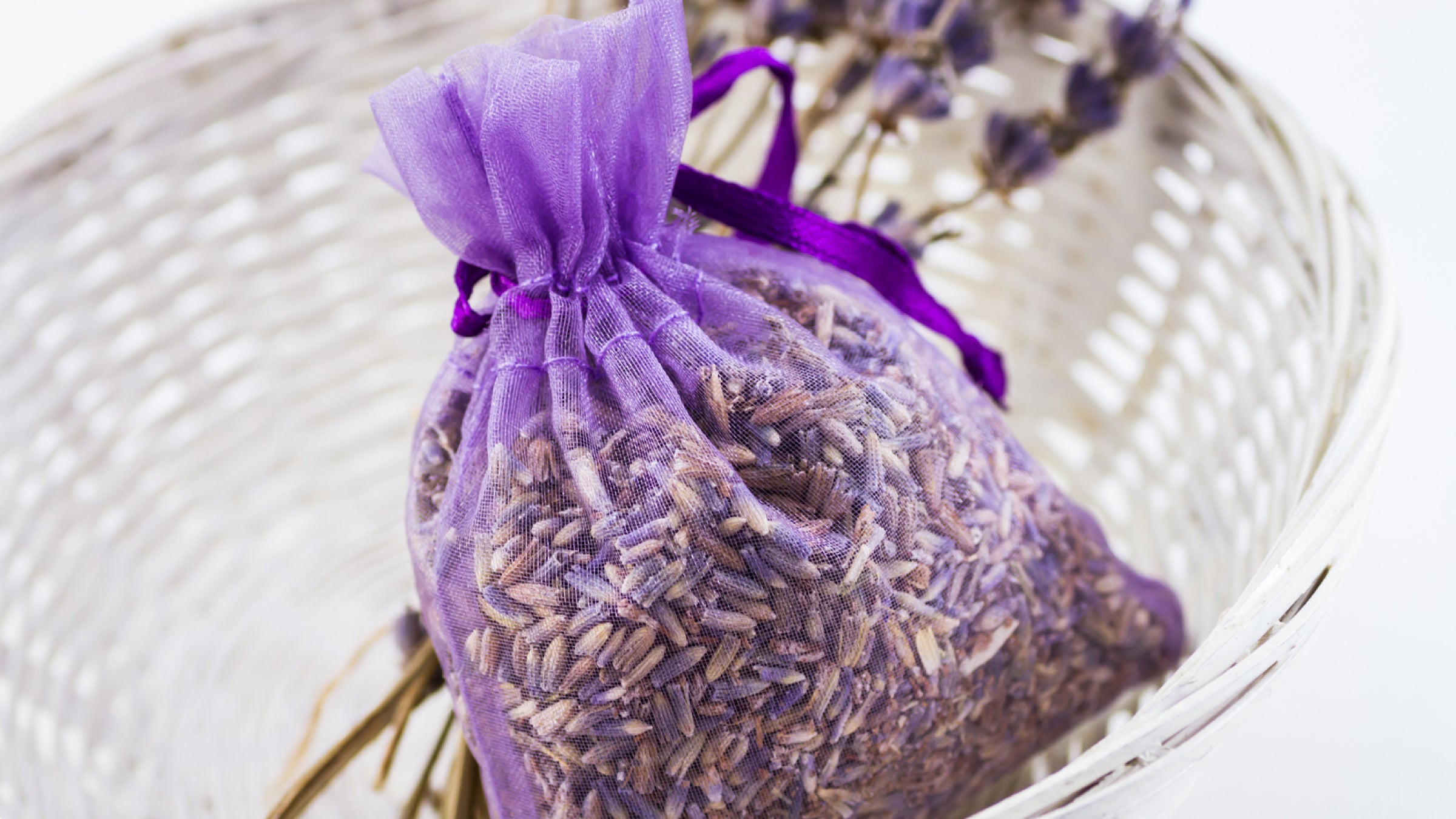 A bag of dried lavender petals sits in a white basket with a few sprigs of lavender