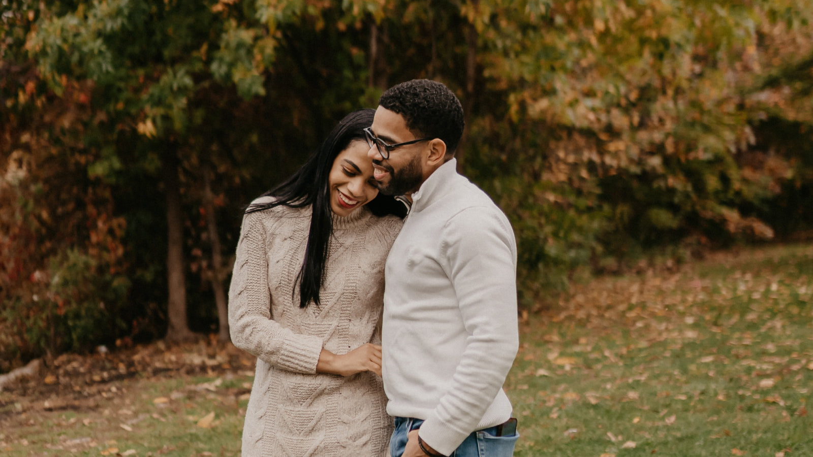 A black couple smiles wearing fall sweaters during autumn