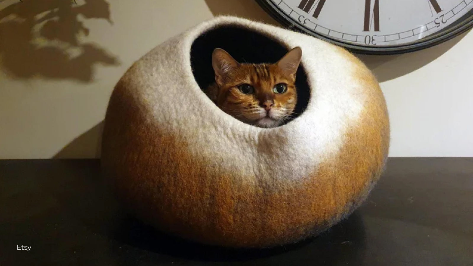A brown cat pokes its head out from a felted cat cave