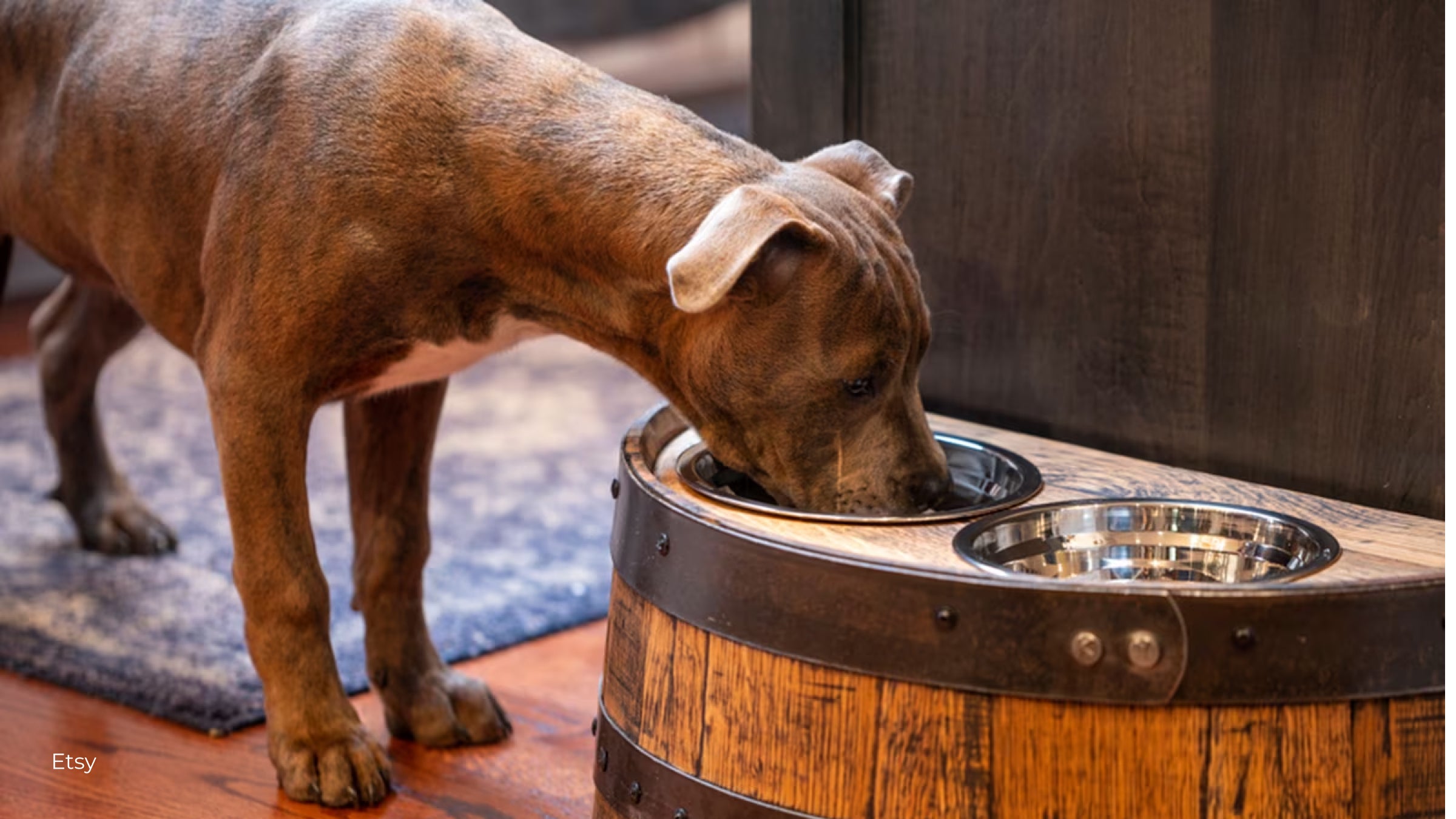 A brown dog eats out of a raised pet bowl set made out of a whiskey barrel