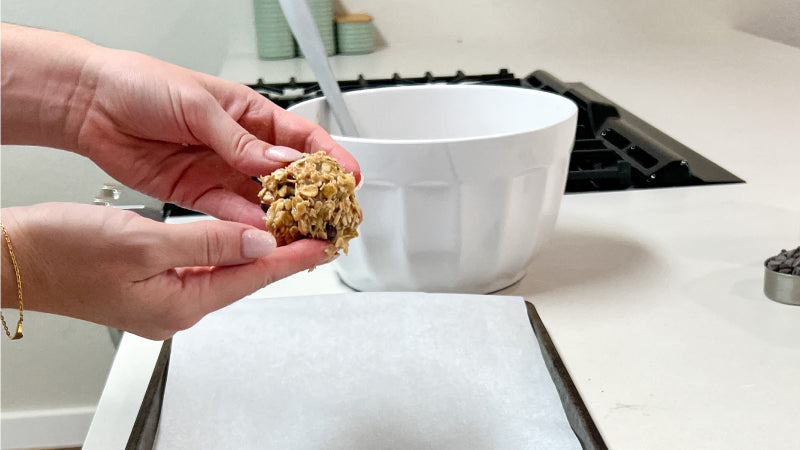 A cookie dough ball is held up by two hands