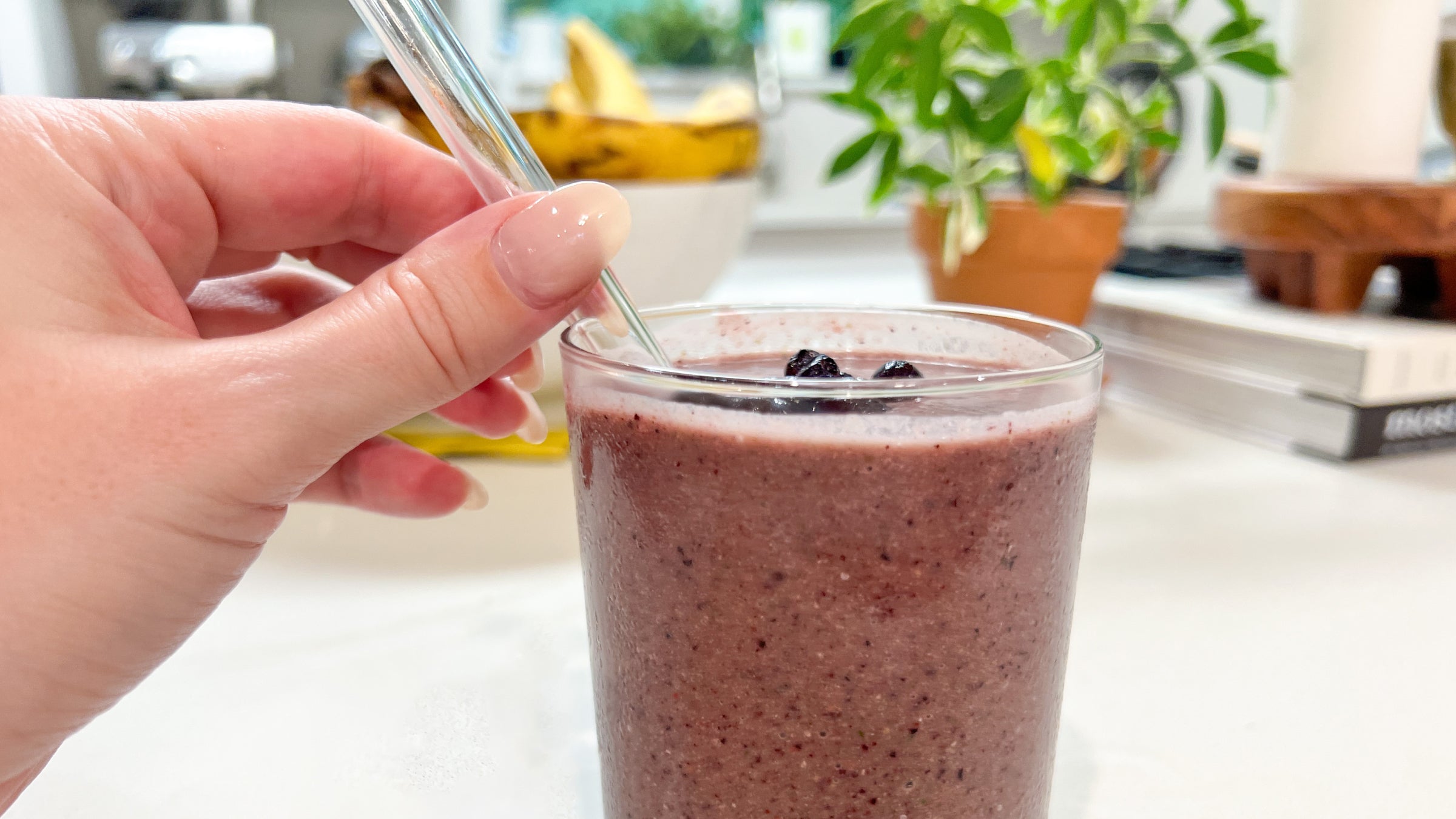 A female hand holding a glass straw in a cup filled with a purple smoothie