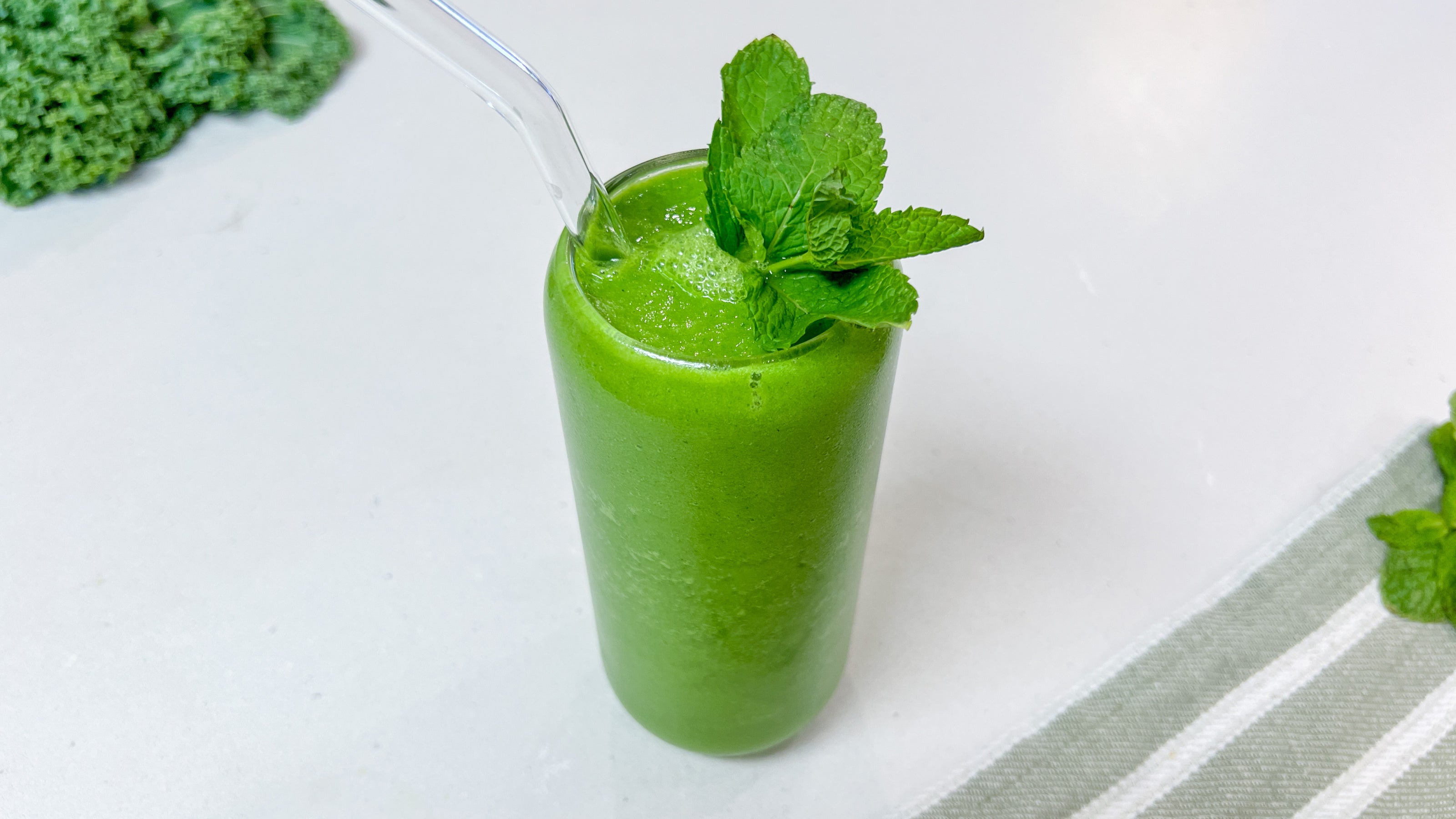 A green smoothie in a glass next to a striped green gray and white towel