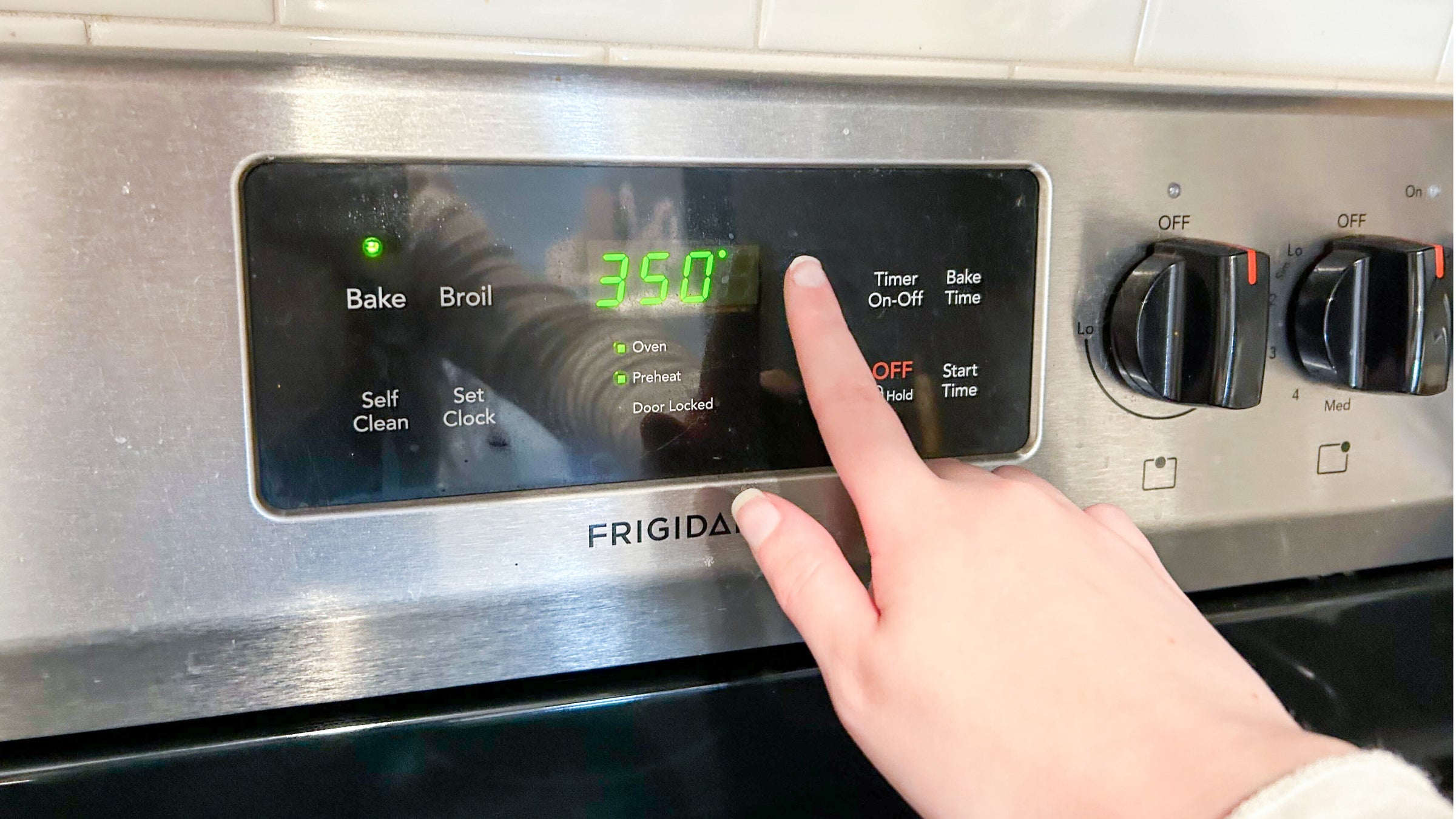 A hand preheats an oven to 350 degrees