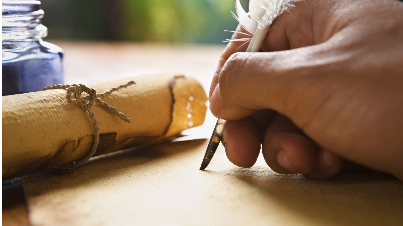 A hand writing with a quill pen with a paper roll and ink well behind