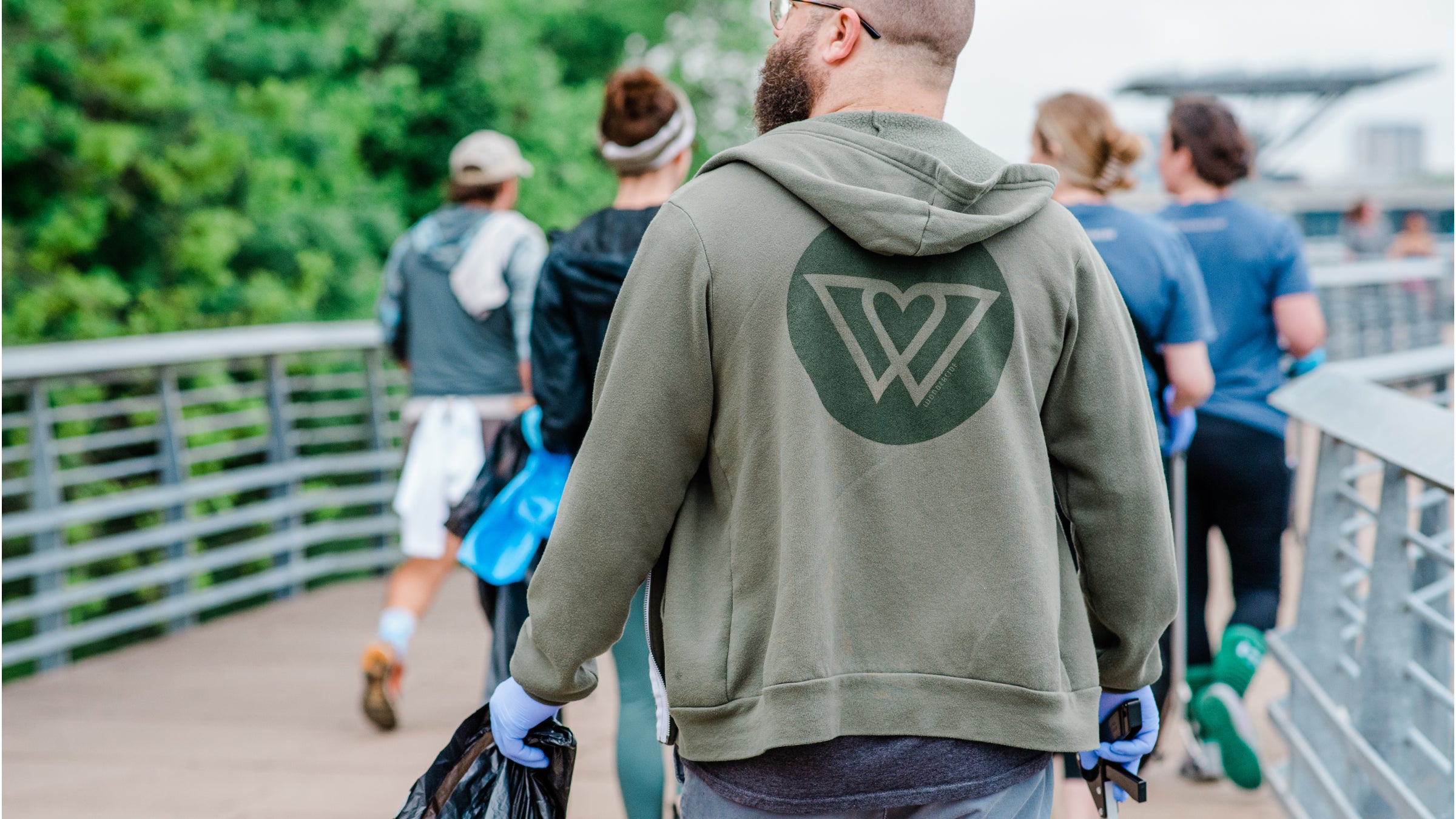 A man picks up trash along the Austin waterway while wearing a Wondercide hoodie