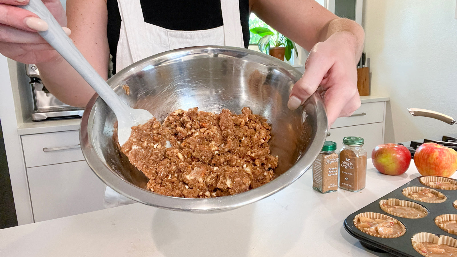 A person presenting apple muffin mixture in a silver bowl to show consistency