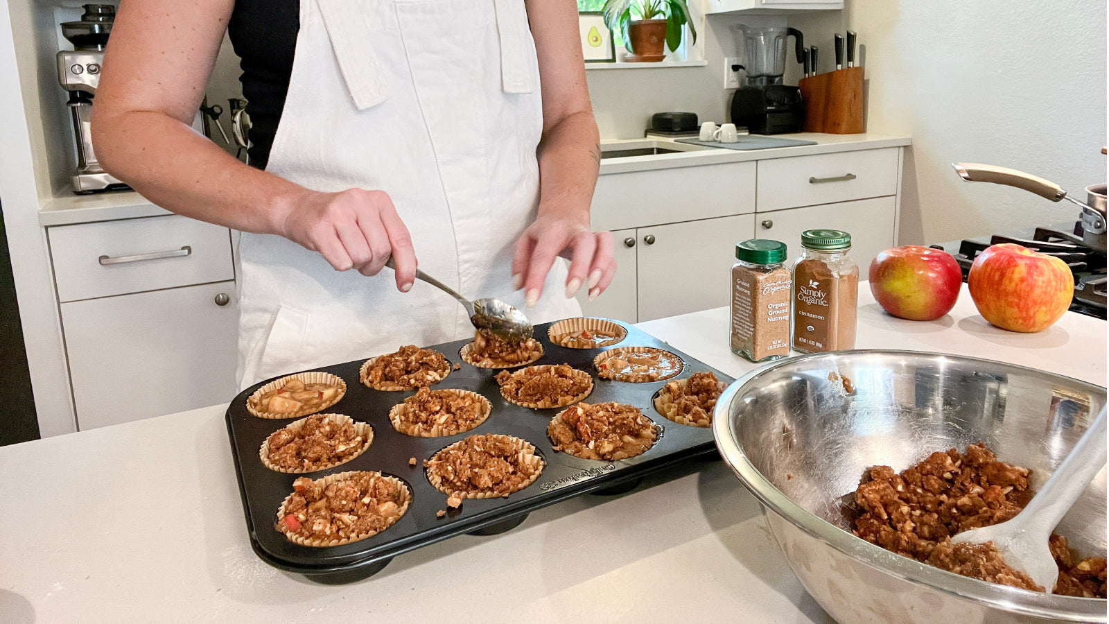 A person spooning apple muffin batter and crumble topping into muffin cups