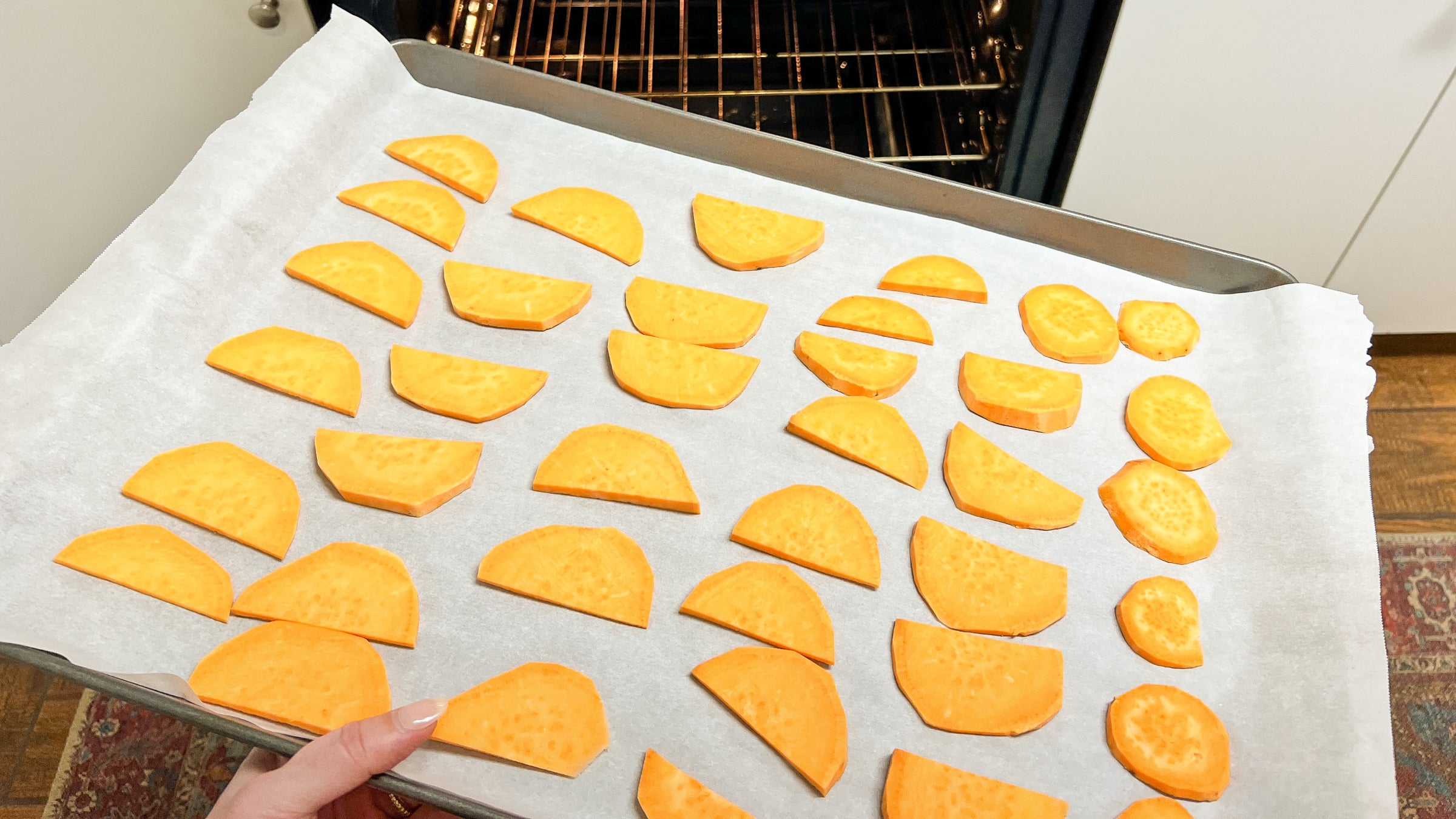 A tray of sweet potato slices on parchment paper goes into an oven