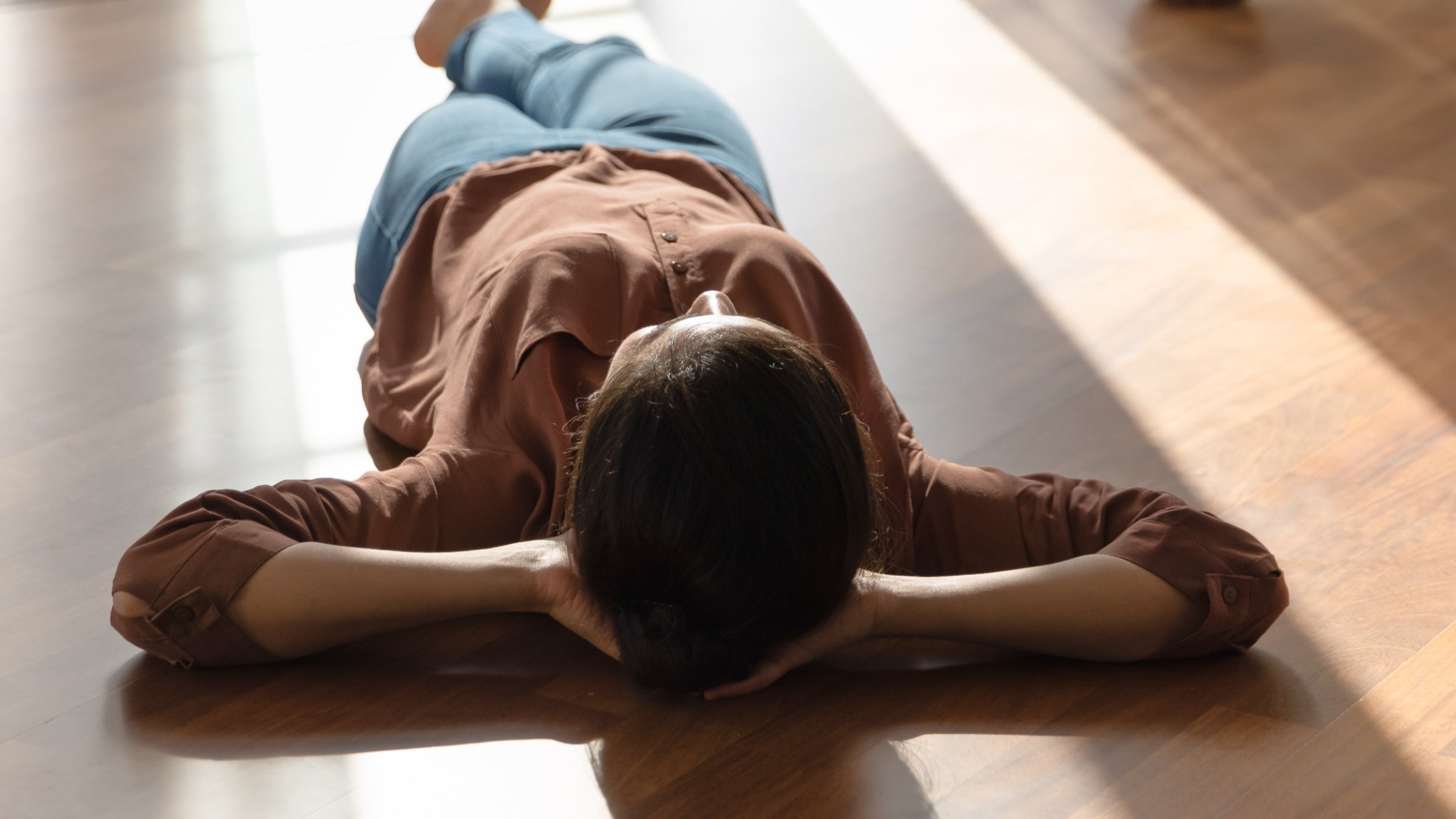 A woman in a copper color shirt lying on the floor basking in sunlight