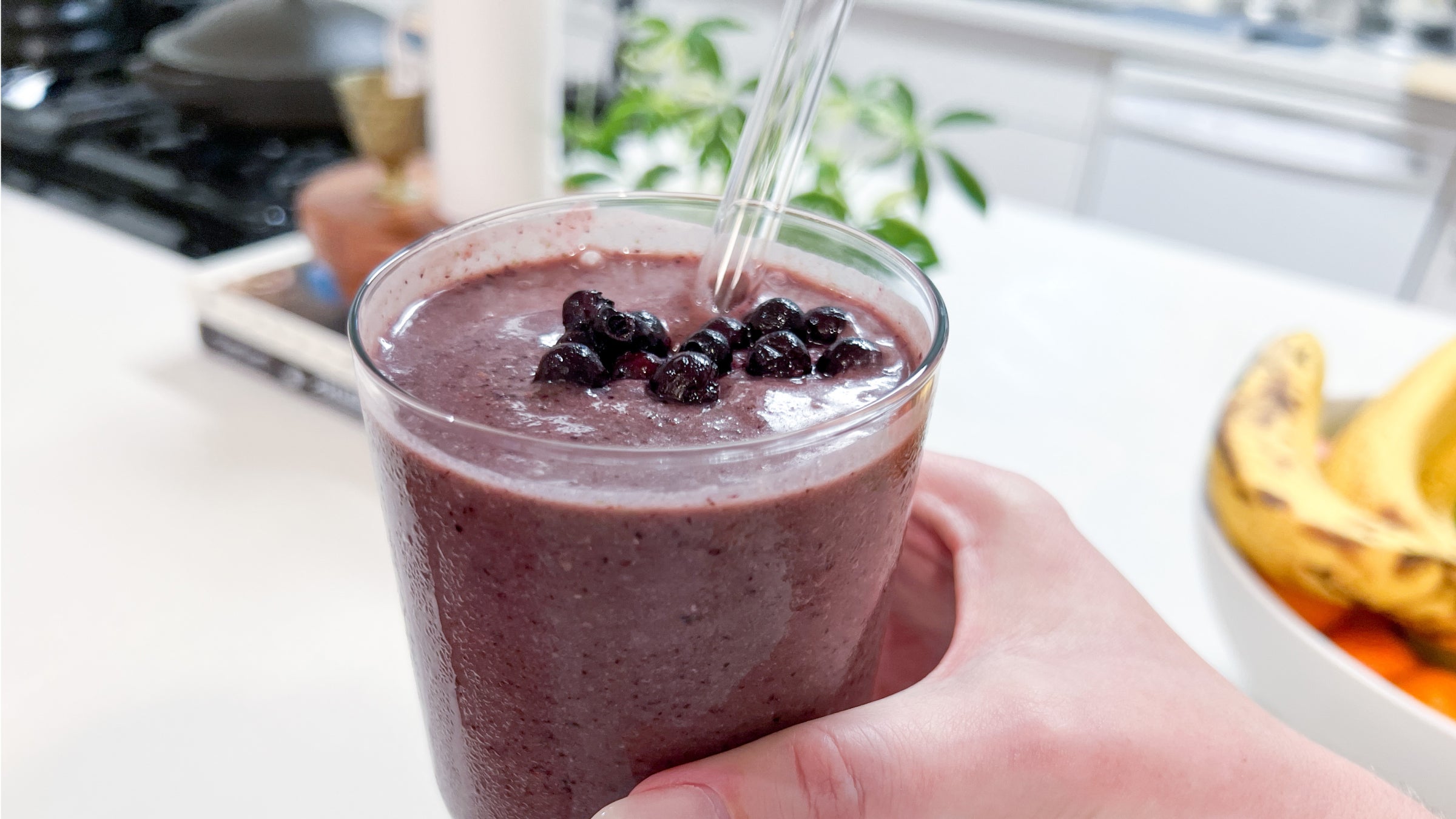 A woman toasting with a purple smoothie in a glass cup with blueberries on top