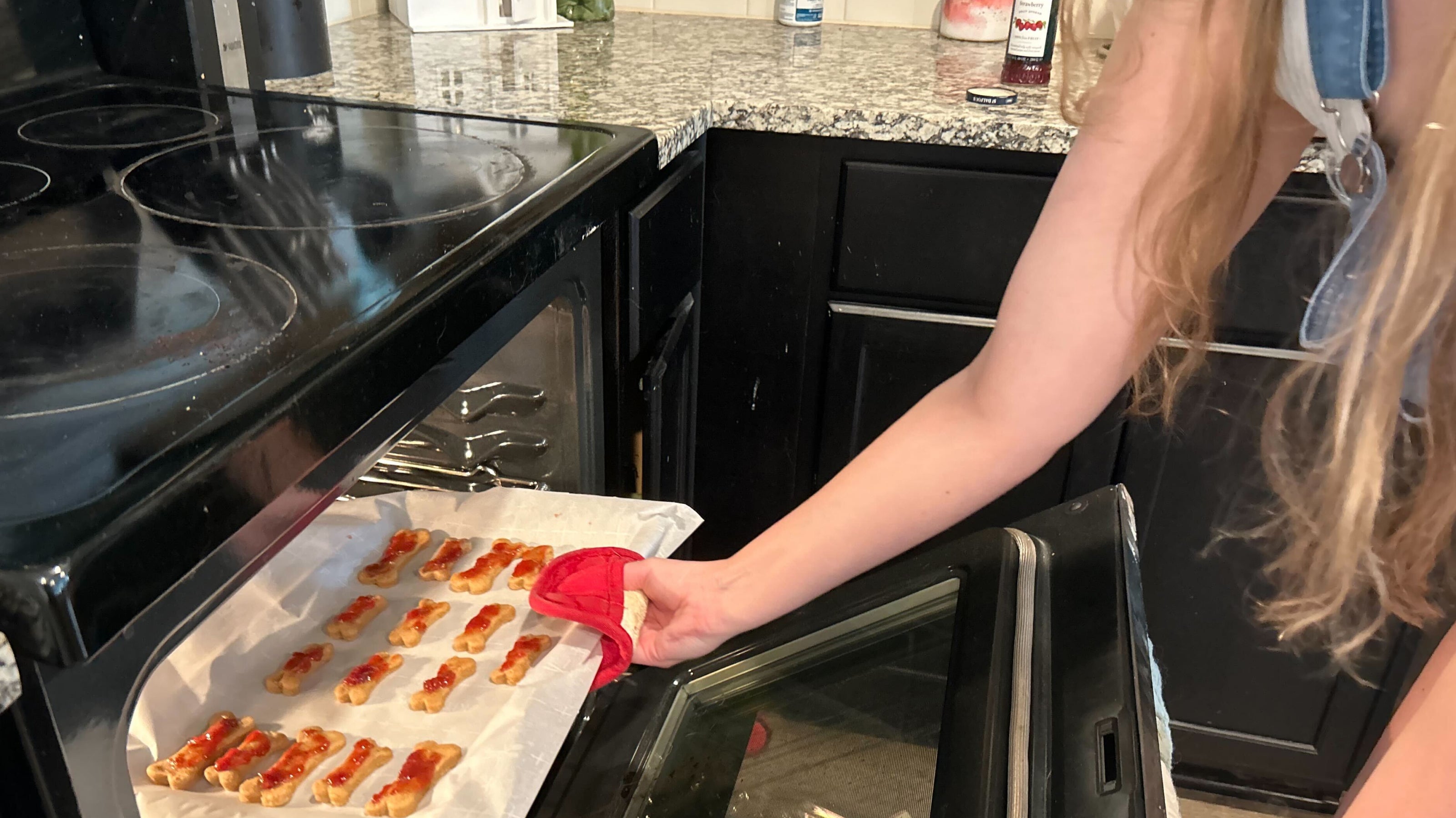 A woman with long blonde hair placing peanut butter and jelly dog treats in the oven