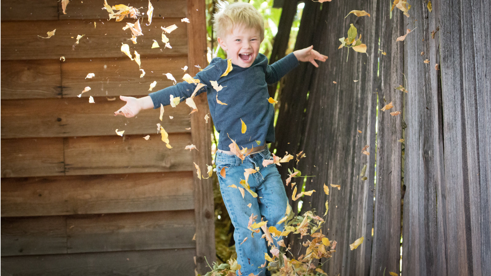 A young boy jumps in a leaf pile