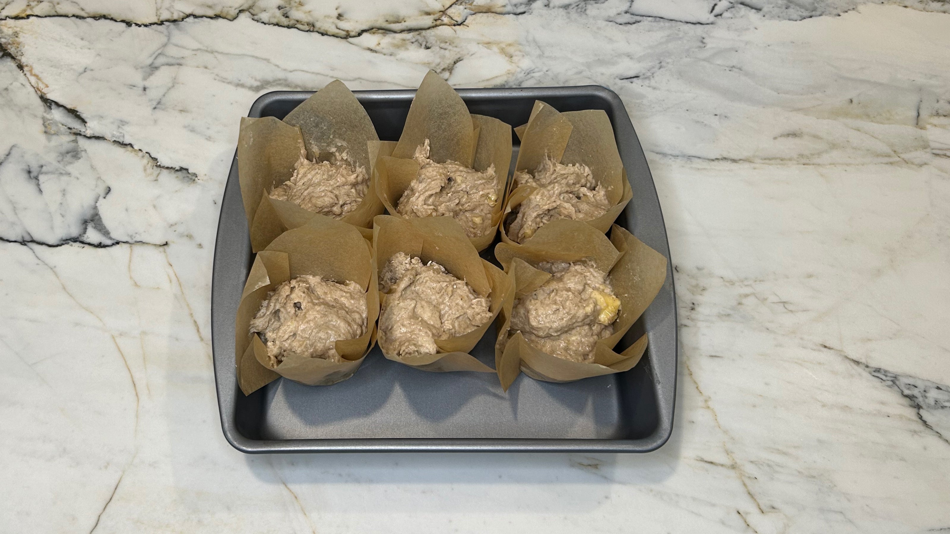 Apple banana muffin batter in parchment muffin papers in a baking tray