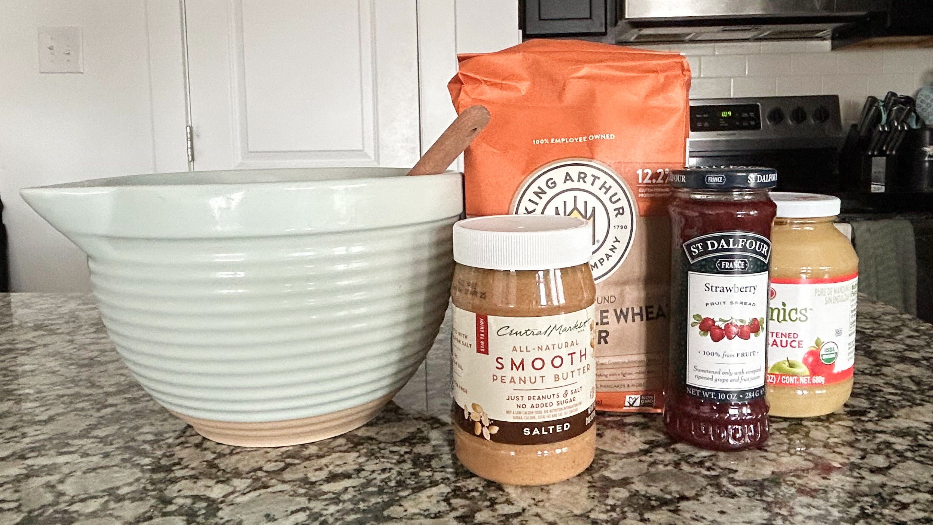 Ingredients for PB&J dog treats placed on a countertop next to a mixing bowl.