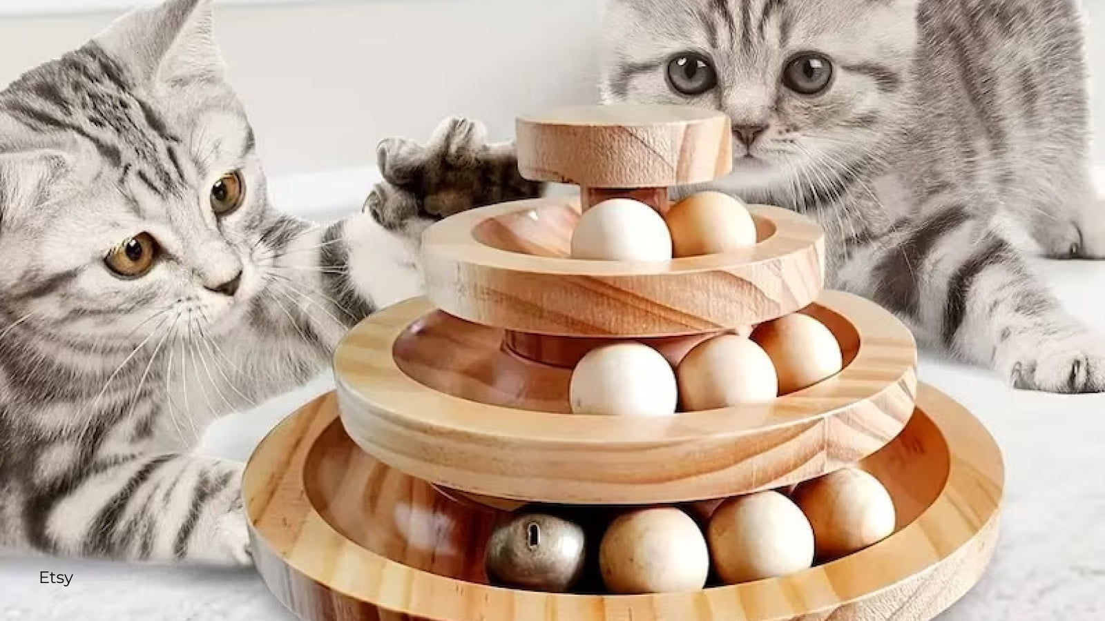 Two light gray kittens play with a three-tier wooden cat toy with balls