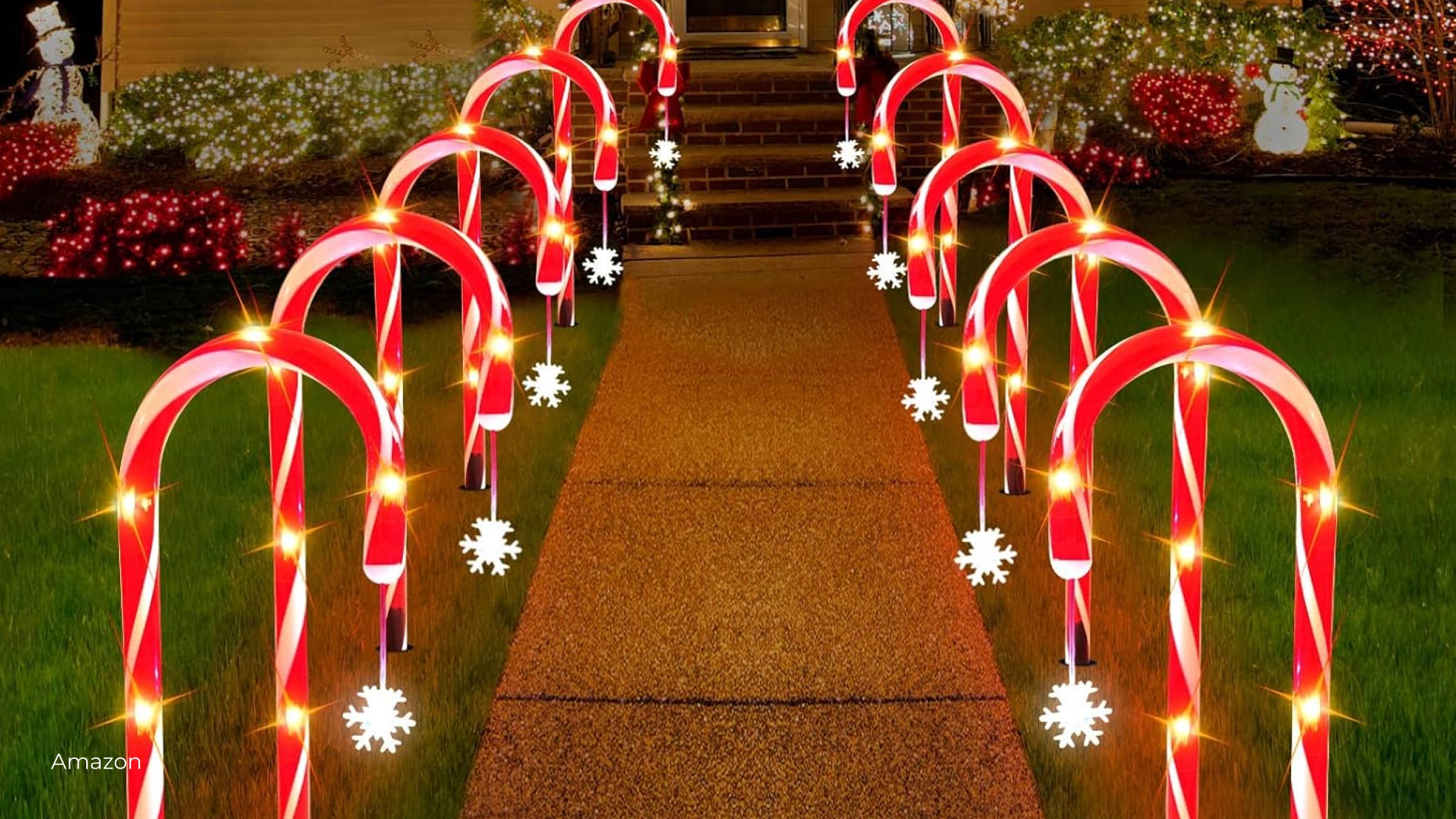 Two rows of illuminated peppermint candy canes line a walkway up to a house