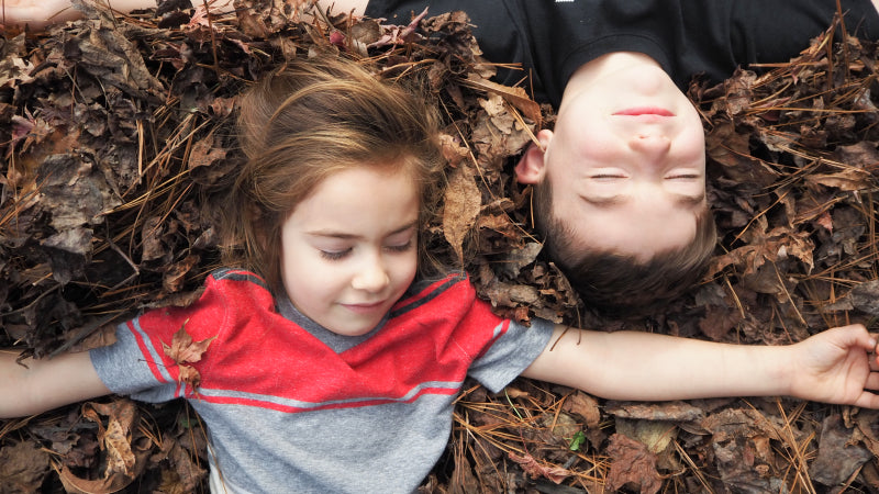 Two young kids lay on a bed of leaves outside