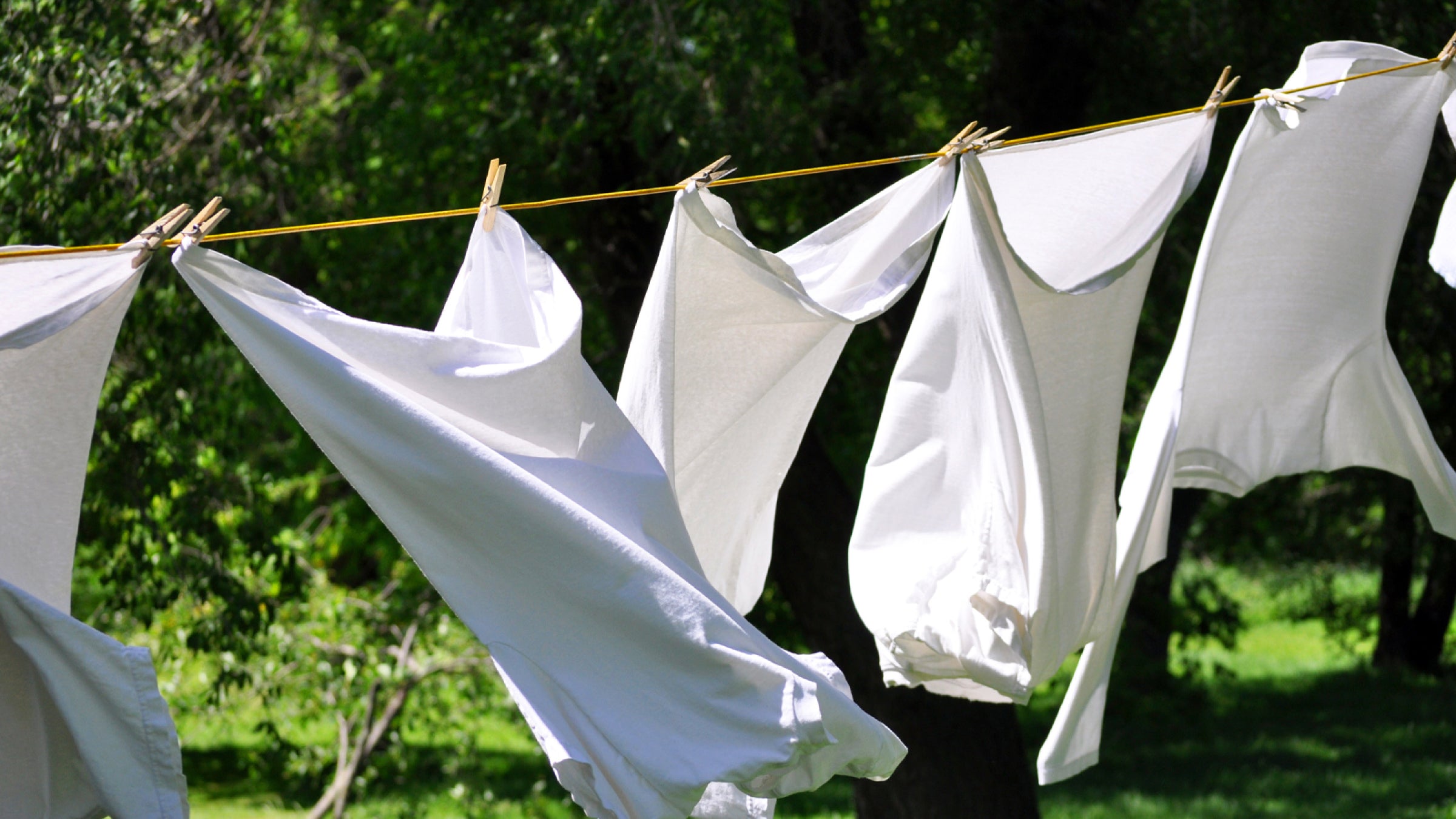 White garments hung on a clothes line outdoors with greenery in the background
