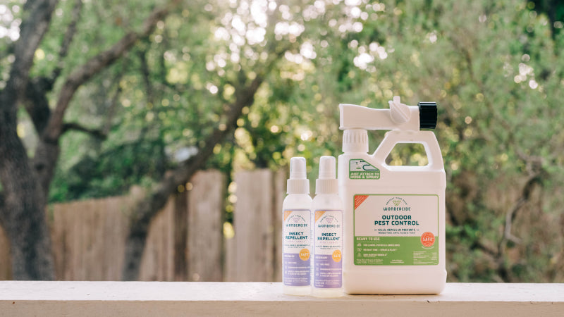 Wondercide yard spray and insect repellent sprays placed on a wood railing outdoors