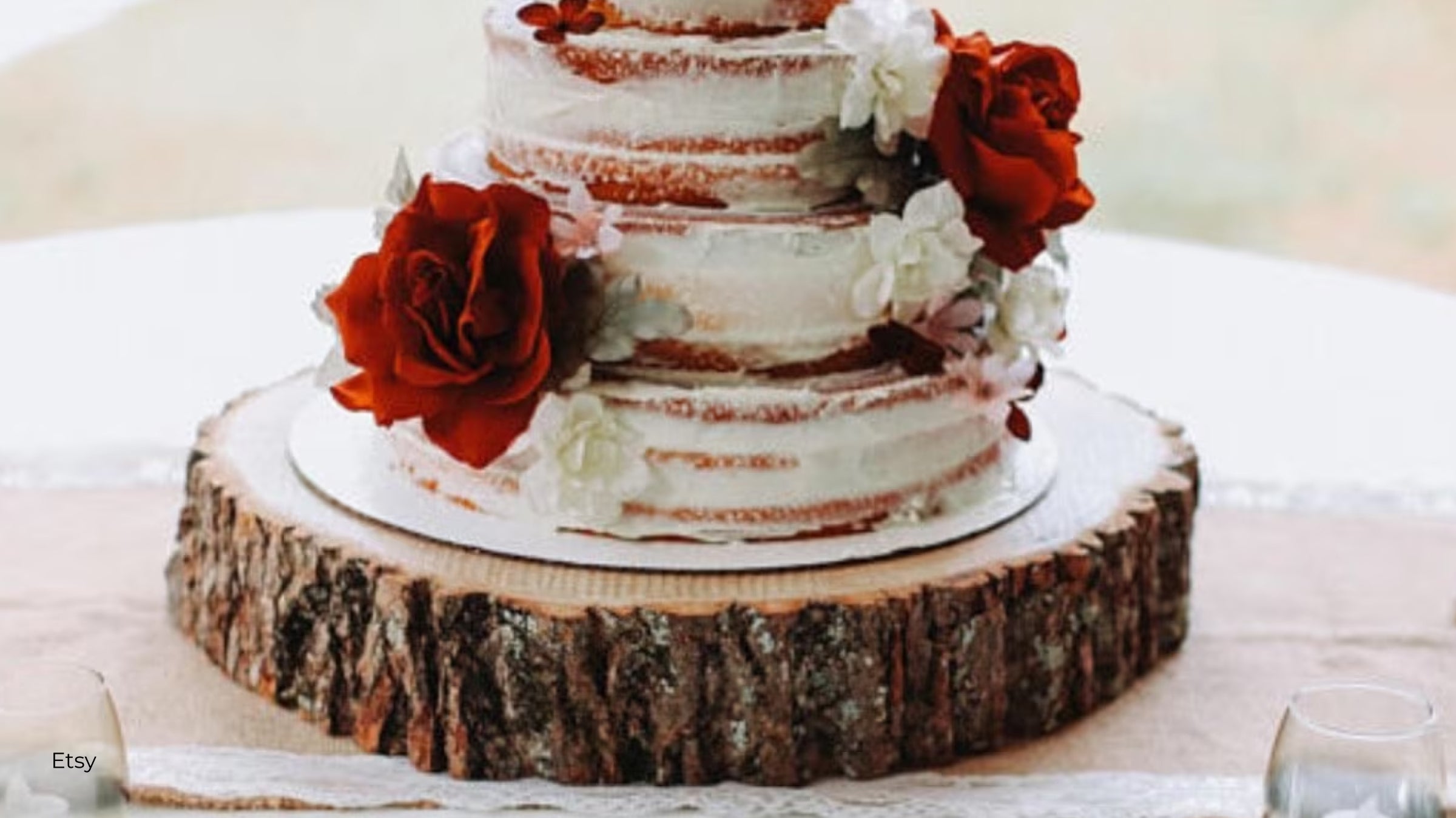 Wood cake stand from Etsy with a white cake on top and two red roses