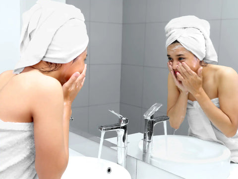 Woman cleaning her face in front of mirror