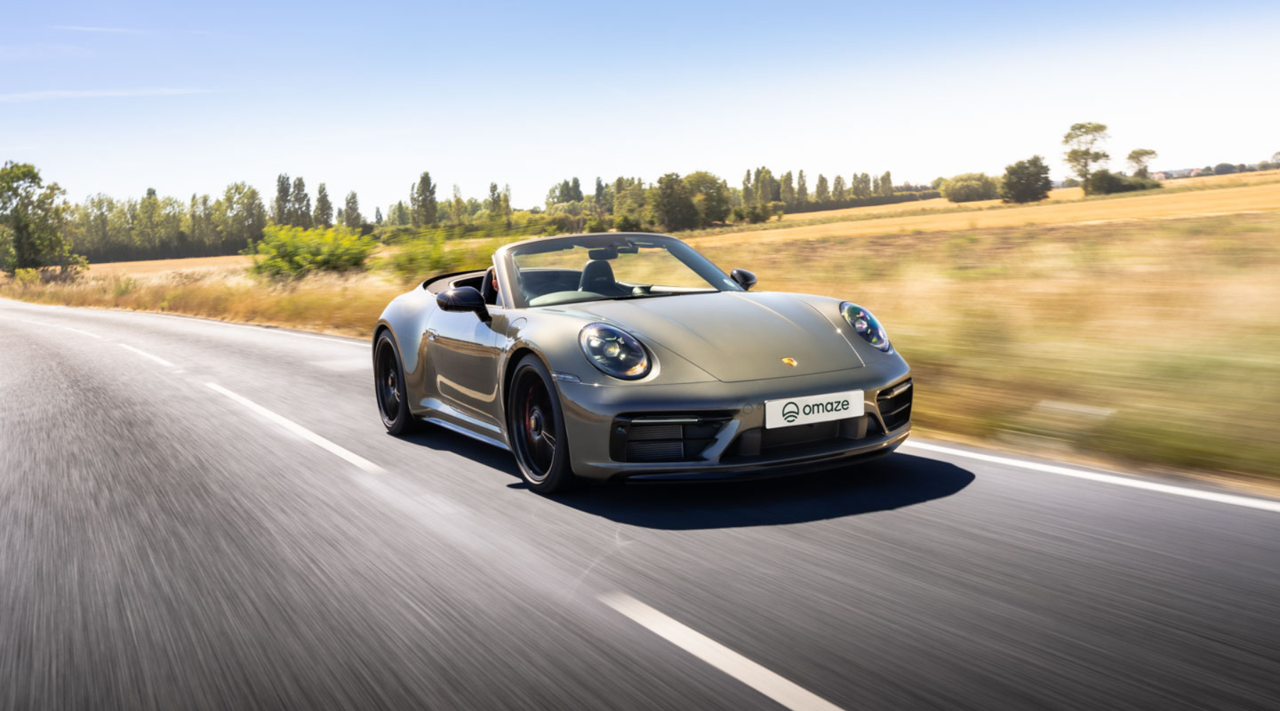Omaze Million Pound House Draw Marbella Win a Porsche 911 GTS. Porsche being driven along the road with blurred trees and fields in the background