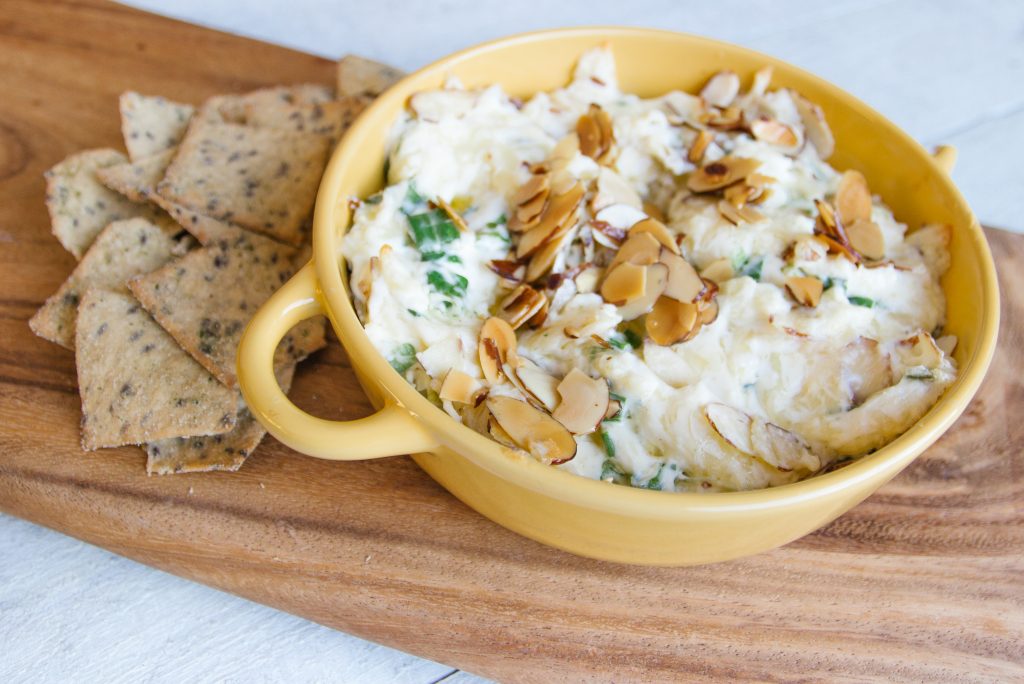 Swiss cheese dip with almond slivers on a wooden cheese board