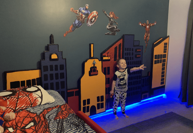 Superhero City finished buildings installed with LED light strip underneath glowing blue with Baby D smiling and shooting his spider webs