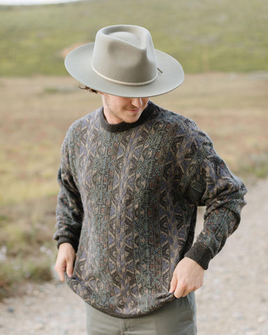 Man outside grabbing the bottom of his patterned knitted sweater in a felt fedora men’s casual hat