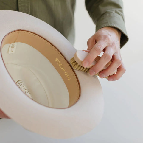 Man using a hat brush to clean fedora hat