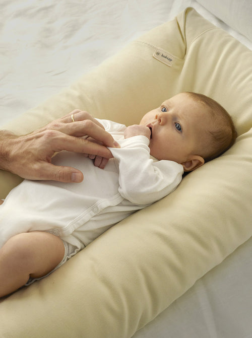 Ein Baby liegt in einem beigen loulouby Babynest und wird geliebkost