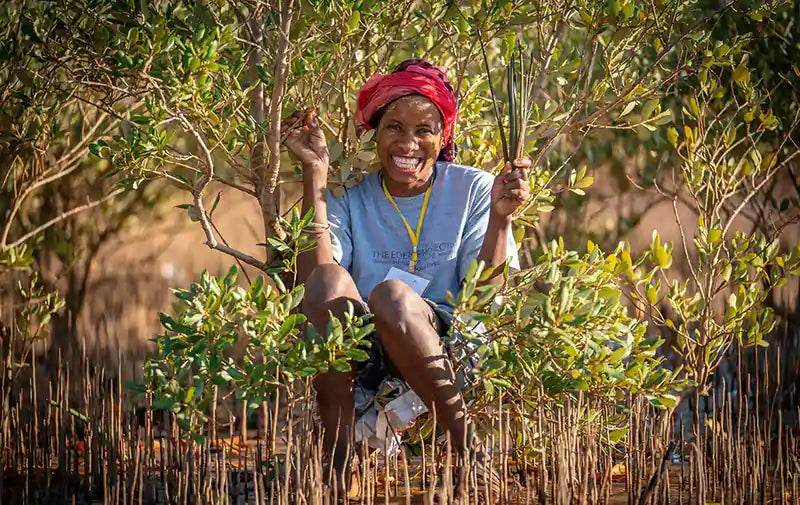 Eine lächelnde schwarze Frau von den Eden Reforestation Projects sitzt in der Natur