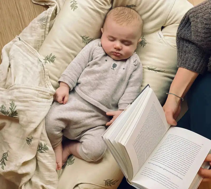 Eine Mutter liest während ihr Baby in einem Babynest schläft