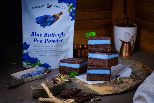 Blue Matcha Mint Brownies stacked on a cutting board in front of Ancient Choice Butterfly Pea Flower Powder