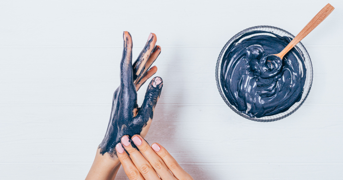 A woman spreading activated charcoal mask on her hands.