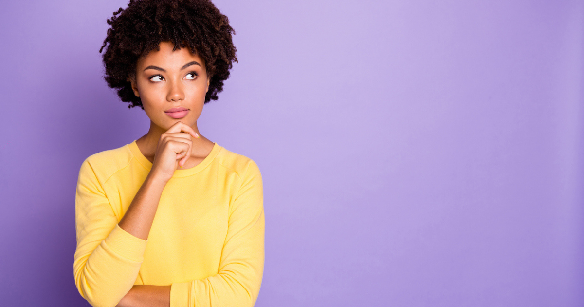 A black woman in a yellow shirt against a purple backgroun with a curious look on her face.