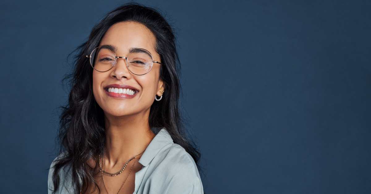 A smiling woman in glasses against a dark blue background who's happy she got her vaginal odor issue under control with Goddess of the Sea.