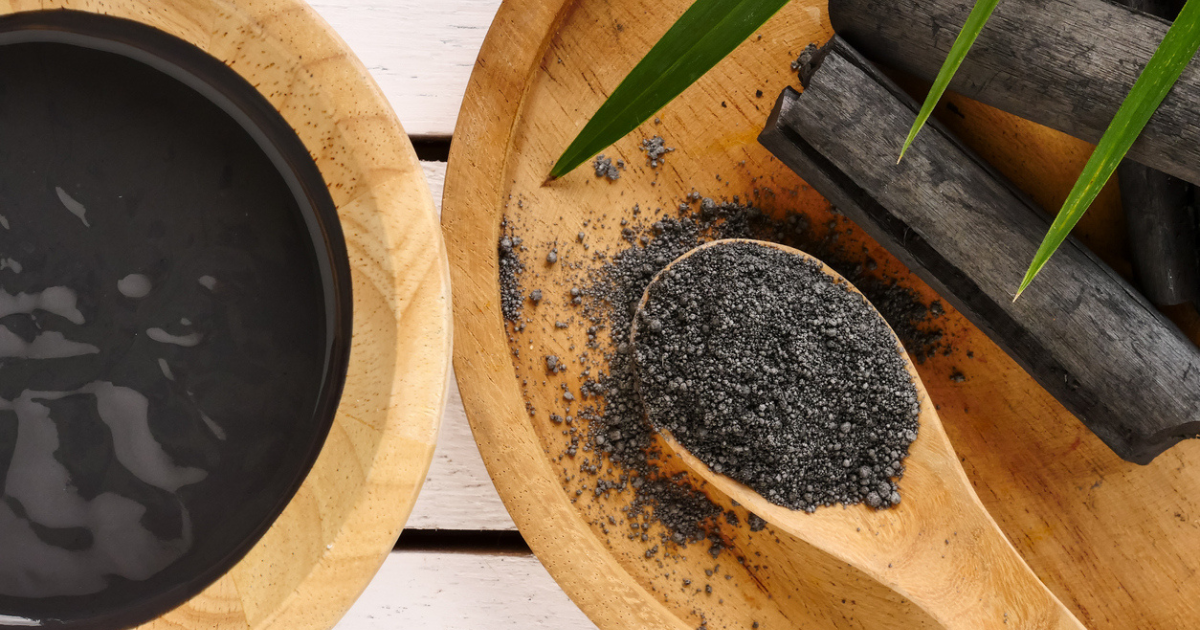 A bowl filled with activated charcoal face mask and a spoon filled with activated charcoal particles.