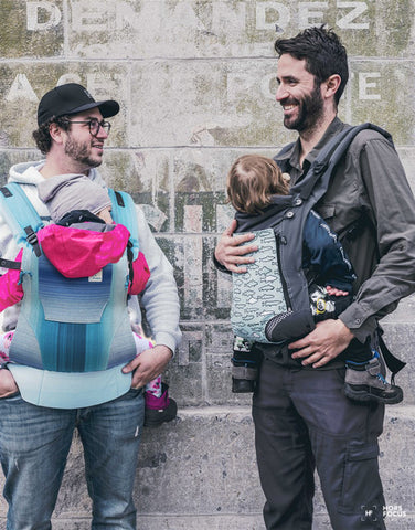 Deux papas se promènent avec leurs bébés en porte-bébé Bambino.