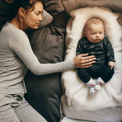 Une maman dort en cododo avec son bébé disposé dans un lit à côté d’elle.