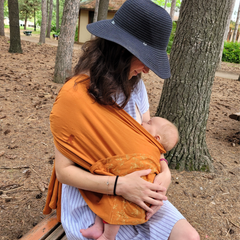 Une maman allaite en portage avec le vêtement peau-à-peau Snüg.