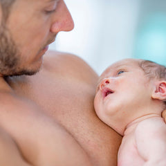 Un papa pratique le peau à peau avec son enfant. Le bébé est positionné dénudé sur la poitrine nue du parent.