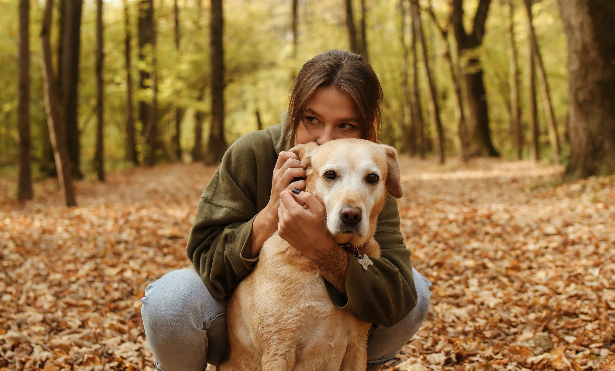 A young woman hugs a white dog from behind during a fall in the forest