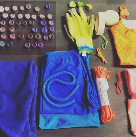 various items on desk in colourful palette, blue, lime yellow, orange, various shades of purple and brown, rope, gloves, shorts are on the desk