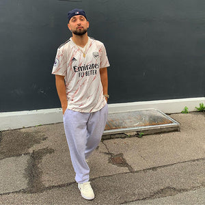 man stood cream arsenal sports top grey joggers cream trainers outside